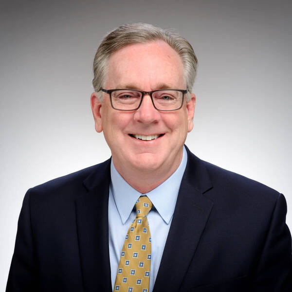 Headshot of Brian Levey, wearing a blue shirt, dark blue suit, and yellow patterned tie.